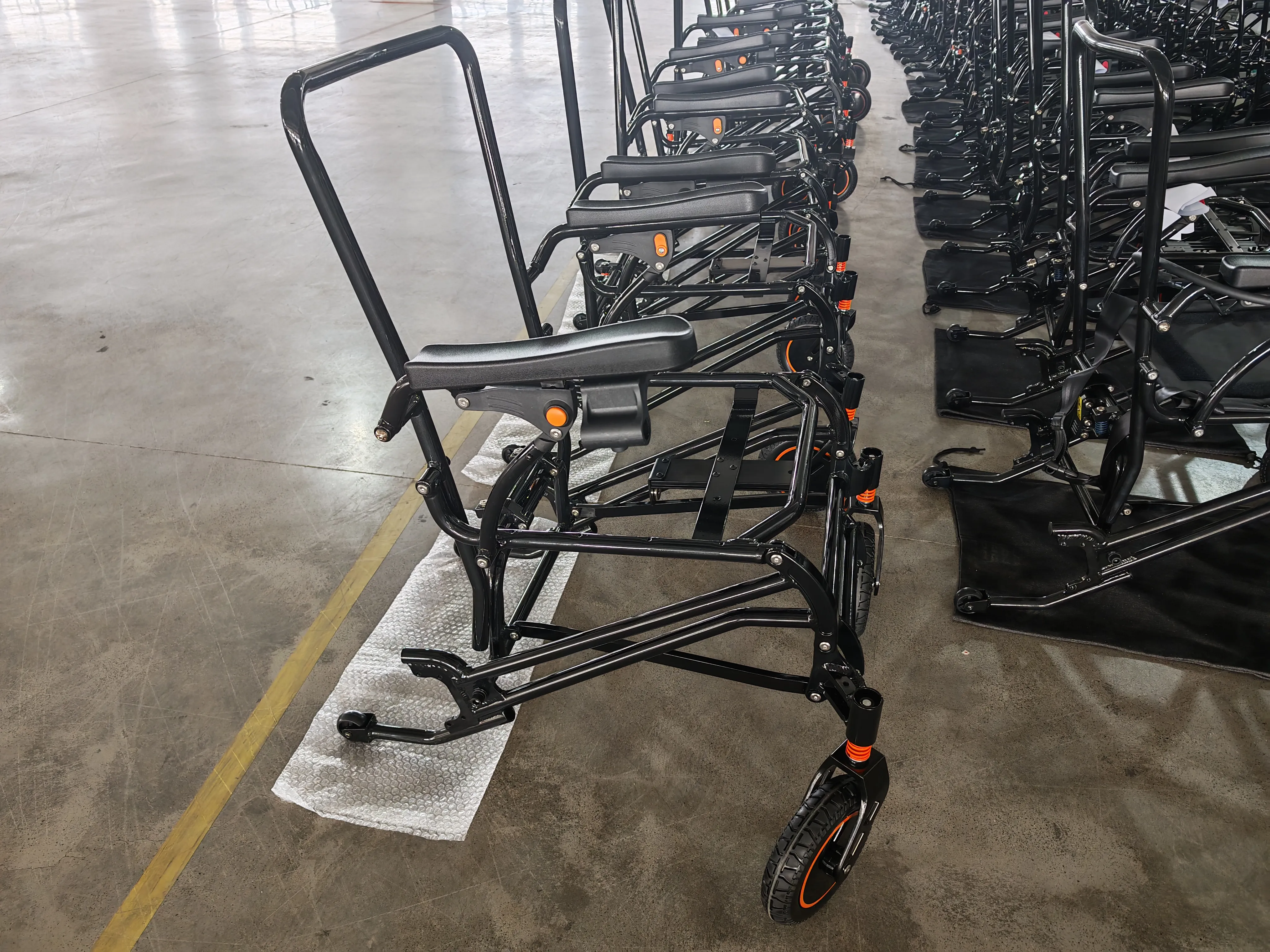 A row of foldable wheelchairs arranged in a factory setting. Each wheelchair features a durable black metal frame with orange highlights, designed for easy folding and storage. The models are equipped with cushioned seats, supportive backrests, and large wheels for smooth mobility, resting on protective mats. Ideal for individuals with limited mobility, these space-saving and high-quality mobility aids are showcased indoors. electric mobility scooter wheelchair, electric chair scooter, chair electric scooter, electric chairs and scooters, scooter electric chair, power chair scooter, power scooter chair, motorized chair scooter, motorized scooter chair, electric wheelchairs and mobility scooters, electric scooter chair for adults, electric chair scooters for adults,electric scooter wheelchair,scooter wheelchair,mobility scooters electric wheelchair,electric wheelchair scooter,wheelchair scooter,chair scooter electric,scooter chair,wheelchair scooters,wheelchairs and scooter,chair scooter electric, electronic wheel chair,  motorized wheel chair,  motor wheel chairs,  electric power chairs for sale,  power chair prices,  motorized wheel chair price,  electric portable wheelchairs,  electric lightweight folding wheelchair,  best motorised wheelchair,  mobile wheelchair,  electric wheel chairs,  power chair for elderly,  power chair for seniors,  electric handicap chair,  power chair cost,  electric mobility chair,  mobility power chair,  power chairs for sale,  electric power chair,  mechanical wheelchair,  mobility electric chair,  e wheelchair,  outdoor power chair,  power chairs for outdoors,  electric wheel chairs for sale,  electric mobility wheelchairs,  electric mobility chairs for adults,  electric mobile chair,  motor assisted wheelchair,  motor powered wheelchair,  power wheel wheelchair,  lightweight folding wheelchair electric,  travel power chair,  compact power chair,  power travel wheelchair,  wheel chairs electric,  Electric Wheelchairs CE, power wheelchair CE, power electric wheelchair CE, Powered Wheelchair CE, electric power wheelchair CE, power chair CE, electric powerchair CE, Motorized Wheelchair CE, Electrically Powered Wheelchair CE, battery operated wheelchair CE, battery powered wheelchairs CE, electric disabled chair CE, electric mobile wheelchair CE, electric mobility wheelchairs CE, electric motorized wheelchair CE, electric power wheelchair CE, electric powered wheelchair CE, electrical wheelchair CE, electronic wheelchair CE, mechanised wheelchair CE, mobility electric wheelchairs CE, motor wheelchair CE, motorised wheelchairs CE, power electric wheelchair CE, rechargeable wheelchair CE, wheel chair electric CE, wheel chair with battery CE, wheelchair battery operated CE, wheelchair electric CE, wheelchair motorized CE, wheelchair with battery CE, Electric Wheelchairs ISO13485, power wheelchair ISO13485, power electric wheelchair ISO13485, Powered Wheelchair ISO13485, electric power wheelchair ISO13485, power chair ISO13485, electric powerchair ISO13485, Motorized Wheelchair ISO13485, Electrically Powered Wheelchair ISO13485, battery operated wheelchair ISO13485, battery powered wheelchairs ISO13485, electric disabled chair ISO13485, electric mobile wheelchair ISO13485, electric mobility wheelchairs ISO13485, electric motorized wheelchair ISO13485, electric power wheelchair ISO13485, electric powered wheelchair ISO13485, electrical wheelchair ISO13485, electronic wheelchair ISO13485, mechanised wheelchair ISO13485, mobility electric wheelchairs ISO13485, motor wheelchair ISO13485, motorised wheelchairs ISO13485, power electric wheelchair ISO13485, rechargeable wheelchair ISO13485, wheel chair electric ISO13485, wheel chair with battery ISO13485, wheelchair battery operated ISO13485, wheelchair electric ISO13485, wheelchair motorized ISO13485, wheelchair with battery ISO13485, folding Electric Wheelchairs, folding power wheelchair, folding power electric wheelchair, folding Powered Wheelchair, folding electric power wheelchair, folding power chair, folding electric powerchair, folding Motorized Wheelchair, folding Electrically Powered Wheelchair, folding battery operated wheelchair, folding battery powered wheelchairs, folding electric disabled chair, folding electric mobile wheelchair, folding electric mobility wheelchairs, folding electric motorized wheelchair, folding electric power wheelchair, folding electric powered wheelchair, folding electrical wheelchair, folding electronic wheelchair, folding mechanised wheelchair, folding mobility electric wheelchairs, folding motor wheelchair, folding motorised wheelchairs, folding power electric wheelchair, folding rechargeable wheelchair, folding wheel chair electric, folding wheel chair with battery, folding wheelchair battery operated, folding wheelchair electric, folding wheelchair motorized, folding wheelchair with battery, foldable Electric Wheelchairs, foldable power wheelchair, foldable power electric wheelchair, foldable Powered Wheelchair, foldable, electric power wheelchair, foldable power chair, foldable electric powerchair, foldable Motorized Wheelchair, foldable Electrically Powered Wheelchair, foldable battery operated wheelchair, foldable battery powered wheelchairs, foldable electric disabled chair, foldable electric mobile wheelchair, foldable electric mobility wheelchairs, foldable electric motorized wheelchair, foldable electric power wheelchair, foldable electric powered wheelchair, foldable electrical wheelchair, foldable electronic wheelchair, foldable mechanised wheelchair, foldable mobility electric wheelchairs, foldable motor wheelchair, foldable motorised wheelchairs, foldable power electric wheelchair, foldable rechargeable wheelchair, foldable wheel chair electric, foldable wheel chair with battery, foldable wheelchair battery operated, foldable wheelchair electric, foldable wheelchair motorized, foldable wheelchair with battery, portable Electric Wheelchairs, portable power wheelchair, portable power electric wheelchair, portable Powered Wheelchair, portable electric power wheelchair, portable power chair, portable electric powerchair, portable Motorized Wheelchair, portable Electrically Powered Wheelchair, portable battery operated wheelchair, portable battery powered wheelchairs, portable electric disabled chair, portable electric mobile wheelchair, portable electric mobility wheelchairs, portable electric motorized wheelchair, portable electric power wheelchair, portable electric powered wheelchair, portable electrical wheelchair, portable electronic wheelchair, portable mechanised wheelchair, portable mobility electric wheelchairs, portable motor wheelchair, portable motorised wheelchairs, portable power electric wheelchair, portable rechargeable wheelchair, portable wheel chair electric, portable wheel chair with battery, portable wheelchair battery operated, portable wheelchair electric, portable wheelchair motorized, portable wheelchair with battery, compact Electric Wheelchairs, compact power wheelchair, compact power electric wheelchair, compact Powered Wheelchair, compact electric power wheelchair, compact power chair, compact electric powerchair, compact Motorized Wheelchair, compact Electrically Powered Wheelchair, compact battery operated wheelchair, compact battery powered wheelchairs, compact electric disabled chair, compact electric mobile wheelchair, compact electric mobility wheelchairs, compact electric motorized wheelchair, compact electric power wheelchair, compact electric powered wheelchair, compact electrical wheelchair, compact electronic wheelchair, compact mechanised wheelchair, compact mobility electric wheelchairs, compact motor wheelchair, compact motorised wheelchairs, compact power electric wheelchair, compact rechargeable wheelchair, compact wheel chair electric, compact wheel chair with battery, compact wheelchair battery operated, compact wheelchair electric, compact wheelchair motorized, compact wheelchair with battery, lightweight Electric Wheelchairs, lightweight power wheelchair, lightweight power electric wheelchair, lightweight Powered Wheelchair, lightweight electric power wheelchair, lightweight power chair, lightweight electric powerchair, lightweight Motorized Wheelchair, lightweight Electrically Powered Wheelchair, lightweight battery operated wheelchair, lightweight battery powered wheelchairs, lightweight electric disabled chair, lightweight electric mobile wheelchair, lightweight electric mobility wheelchairs, lightweight electric motorized wheelchair, lightweight electric power wheelchair, lightweight electric powered wheelchair, lightweight electrical wheelchair, lightweight electronic wheelchair, lightweight mechanised wheelchair, lightweight mobility electric wheelchairs, lightweight motor wheelchair, lightweight motorised wheelchairs, lightweight power electric wheelchair, lightweight rechargeable wheelchair, lightweight wheel chair electric, lightweight wheel chair with battery, lightweight wheelchair battery operated, lightweight wheelchair electric, lightweight wheelchair motorized, lightweight wheelchair with battery, Electric Wheelchairs suppliers price, power wheelchair suppliers price, power electric wheelchair suppliers price, Powered Wheelchair suppliers price, electric power wheelchair suppliers price, power chair suppliers price, electric powerchair suppliers price, Motorized Wheelchair suppliers price, Electrically Powered Wheelchair suppliers price, battery operated wheelchair suppliers price, battery powered wheelchairs suppliers price, electric disabled chair suppliers price, electric mobile wheelchair suppliers price, electric mobility wheelchairs suppliers price, electric motorized wheelchair suppliers price, electric power wheelchair suppliers price, electric powered wheelchair suppliers price, electrical wheelchair suppliers price, electronic wheelchair suppliers price, mechanised wheelchair suppliers price, mobility electric wheelchairs suppliers price, motor wheelchair suppliers price, motorised wheelchairs suppliers price, power electric wheelchair suppliers price, rechargeable wheelchair suppliers price, wheel chair electric suppliers price, wheel chair with battery suppliers price, wheelchair battery operated suppliers price, wheelchair electric suppliers price, wheelchair motorized suppliers price, wheelchair with battery suppliers price, electric travel Wheelchairs, power travel wheelchair, power electric travel wheelchair, Powered travel Wheelchair, electric power travel wheelchair, power travel chair, electric travel powerchair, Motorized travel Wheelchair, Electrically Powered travel Wheelchair, battery operated travel wheelchair, battery powered travel wheelchairs, electric disabled chair for travelling, electric mobile travel  wheelchair, electric mobility travel wheelchairs, electric motorized travel wheelchair, electric power travel wheelchair, electric powered travel wheelchair, electrical travel wheelchair, electronic travel wheelchair, mechanised travel wheelchair, mobility electric travel wheelchairs, motor travel wheelchair, motorised travel wheelchairs, power electric travel wheelchair, rechargeable travel wheelchair, travel wheel chair electric, travel wheel chair with battery, travel wheelchair battery operated, travel wheelchair electric, travel wheelchair motorized, travel wheelchair with battery, Electric Wheelchairs for seniors, power wheelchair for seniors, power electric wheelchair for seniors, Powered Wheelchair for seniors, electric power wheelchair for seniors, power chair for seniors, electric powerchair for seniors, Motorized Wheelchair for seniors, Electrically Powered Wheelchair for seniors, battery operated wheelchair for seniors, battery powered wheelchairs for seniors, electric disabled chair for seniors, electric mobile wheelchair for seniors, electric mobility wheelchairs for seniors, electric motorized wheelchair for seniors, electric power wheelchair for seniors, electric powered wheelchair for seniors, electrical wheelchair for seniors, electronic wheelchair for seniors, mechanised wheelchair for seniors, mobility electric wheelchairs for seniors, motor wheelchair for seniors, motorised wheelchairs for seniors, power electric wheelchair for seniors, rechargeable wheelchair for seniors, wheel chair electric for seniors, wheel chair with battery for seniors, wheelchair battery operated for seniors, wheelchair electric for seniors, wheelchair motorized for seniors, wheelchair with battery for seniors, Electric Wheelchairs for elderly, power wheelchair for elderly, power electric wheelchair for elderly, Powered Wheelchair for elderly, electric power wheelchair for elderly, power chair for elderly, electric powerchair for elderly, Motorized Wheelchair for elderly, Electrically Powered Wheelchair for elderly, battery operated wheelchair for elderly, battery powered wheelchairs for elderly, electric disabled chair for elderly, electric mobile wheelchair for elderly, electric mobility wheelchairs for elderly, electric motorized wheelchair for elderly, electric power wheelchair for elderly, electric powered wheelchair for elderly, electrical wheelchair for elderly, electronic wheelchair for elderly, mechanised wheelchair for elderly, mobility electric wheelchairs for elderly, motor wheelchair for elderly, motorised wheelchairs for elderly, power electric wheelchair for elderly, rechargeable wheelchair for elderly, wheel chair electric for elderly, wheel chair with battery for elderly, wheelchair battery operated for elderly, wheelchair electric for elderly, wheelchair motorized for elderly, wheelchair with battery for elderly, Electric Wheelchairs for handicapped, power wheelchair for handicapped, power electric wheelchair for handicapped, Powered Wheelchair for handicapped, electric power wheelchair for handicapped, power chair for handicapped, electric powerchair for handicapped, Motorized Wheelchair for handicapped, Electrically Powered Wheelchair for handicapped, battery operated wheelchair for handicapped, battery powered wheelchairs for handicapped, electric disabled chair for handicapped, electric mobile wheelchair for handicapped, electric mobility wheelchairs for handicapped, electric motorized wheelchair for handicapped, electric power wheelchair for handicapped, electric powered wheelchair for handicapped, electrical wheelchair for handicapped, electronic wheelchair for handicapped, mechanised wheelchair for handicapped, mobility electric wheelchairs for handicapped, motor wheelchair for handicapped, motorised wheelchairs for handicapped, power electric wheelchair for handicapped, rechargeable wheelchair for handicapped, wheel chair electric for handicapped, wheel chair with battery for handicapped, wheelchair battery operated for handicapped, wheelchair electric for handicapped, wheelchair motorized for handicapped, wheelchair with battery for handicapped, Electric Wheelchairs for adults, power wheelchair for adults, power electric wheelchair for adults, Powered Wheelchair for adults, electric power wheelchair for adults, power chair for adults, electric powerchair for adults, Motorized Wheelchair for adults, Electrically Powered Wheelchair for adults, battery operated wheelchair for adults, battery powered wheelchairs for adults, electric disabled chair for adults, electric mobile wheelchair for adults, electric mobility wheelchairs for adults, electric motorized wheelchair for adults, electric power wheelchair for adults, electric powered wheelchair for adults, electrical wheelchair for adults, electronic wheelchair for adults, mechanised wheelchair for adults, mobility electric wheelchairs for adults, motor wheelchair for adults, motorised wheelchairs for adults, power electric wheelchair for adults, rechargeable wheelchair for adults, wheel chair electric for adults, wheel chair with battery for adults, wheelchair battery operated for adults, wheelchair electric for adults, wheelchair motorized for adults, wheelchair with battery for adults, Electric Wheelchairs for old people, power wheelchair for old people, power electric wheelchair for old people, Powered Wheelchair for old people, electric power wheelchair for old people, power chair for old people, electric powerchair for old people, Motorized Wheelchair for old people, Electrically Powered Wheelchair for old people, battery operated wheelchair for old people, battery powered wheelchairs for old people, electric disabled chair for old people, electric mobile wheelchair for old people, electric mobility wheelchairs for old people, electric motorized wheelchair for old people, electric power wheelchair for old people, electric powered wheelchair for old people, electrical wheelchair for old people, electronic wheelchair for old people, mechanised wheelchair for old people, mobility electric wheelchairs for old people, motor wheelchair for old people, motorised wheelchairs for old people, power electric wheelchair for old people, rechargeable wheelchair for old people, wheel chair electric for old people, wheel chair with battery for old people, wheelchair battery operated for old people, wheelchair electric for old people, wheelchair motorized for old people, wheelchair with battery for old people, Electric handicap Wheelchairs, power wheelchair handicap, power electric wheelchair handicap, Powered handicap Wheelchair, electric power wheelchair handicap, power chair handicap, electric powerchair handicap, Motorized Wheelchair handicap, Electrically Powered Wheelchair handicap, battery operated handicap wheelchair, battery powered wheelchairs handicap, electric disabled chair handicap, electric mobile wheelchair handicap, electric mobility wheelchairs handicap, electric motorized wheelchair handicap, electric power wheelchair handicap, electric powered wheelchair handicap, electrical handicap wheelchair, electronic handicap wheelchair, mechanised wheelchair handicap, mobility electric handicap wheelchairs, motor handicap wheelchair, motorised wheelchairs handicap, power electric handicap wheelchair, rechargeable handicap wheelchair, handicap wheel chair electric, handicap wheel chair with battery, handicap wheelchair battery operated, handicap wheelchair electric, handicap wheelchair motorized, handicap wheelchair with battery, Electric Wheelchairs for disbaled, power wheelchair for disbaled, power electric wheelchair for disbaled, Powered Wheelchair for disbaled, electric power wheelchair for disbaled, power chair for disbaled, electric powerchair for disbaled, Motorized Wheelchair for disbaled, Electrically Powered Wheelchair for disbaled, battery operated wheelchair for disbaled, battery powered wheelchairs for disbaled, electric disabled chair for disbaled, electric mobile wheelchair for disbaled, electric mobility wheelchairs for disbaled, electric motorized wheelchair for disbaled, electric power wheelchair for disbaled, electric powered wheelchair for disbaled, electrical wheelchair for disbaled, electronic wheelchair for disbaled, mechanised wheelchair for disbaled, mobility electric wheelchairs for disbaled, motor wheelchair for disbaled, motorised wheelchairs for disbaled, power electric wheelchair for disbaled, rechargeable wheelchair for disbaled, wheel chair electric for disbaled, wheel chair with battery for disbaled, wheelchair battery operated for disbaled, wheelchair electric for disbaled, wheelchair motorized for disbaled, wheelchair with battery for disbaled, Electric Wheelchairs airline approved, power wheelchair airline approved, power electric wheelchair airline approved, Powered Wheelchair airline approved, electric power wheelchair airline approved, power chair airline approved, electric powerchair airline approved, Motorized Wheelchair airline approved, Electrically Powered Wheelchair airline approved, battery operated wheelchair airline approved, battery powered wheelchairs airline approved, electric disabled chair airline approved, electric mobile wheelchair airline approved, electric mobility wheelchairs airline approved, electric motorized wheelchair airline approved, electric power wheelchair airline approved, electric powered wheelchair airline approved, electrical wheelchair airline approved, electronic wheelchair airline approved, mechanised wheelchair airline approved, mobility electric wheelchairs airline approved, motor wheelchair airline approved, motorised wheelchairs airline approved, power electric wheelchair airline approved, rechargeable wheelchair airline approved, wheel chair electric airline approved, wheel chair with battery airline approved, wheelchair battery operated airline approved, wheelchair electric airline approved, wheelchair motorized airline approved, wheelchair with battery airline approved, Electric Wheelchairs design, power wheelchair design, power electric wheelchair design, Powered Wheelchair design, electric power wheelchair design, power chair design, electric powerchair design, Motorized Wheelchair design, Electrically Powered Wheelchair design, battery operated wheelchair design, battery powered wheelchairs design, electric disabled chair design, electric mobile wheelchair design, electric mobility wheelchairs design, electric motorized wheelchair design, electric power wheelchair design, electric powered wheelchair design, electrical wheelchair design, electronic wheelchair design, mechanised wheelchair design, mobility electric wheelchairs design, motor wheelchair design, motorised wheelchairs design, power electric wheelchair design, rechargeable wheelchair design, wheel chair electric design, wheel chair with battery design, wheelchair battery operated design, wheelchair electric design, wheelchair motorized design, wheelchair with battery design, fully foldableElectric Wheelchairs, power wheelchair fully foldable, power electric wheelchair fully foldable, Powered Wheelchair fully foldable, electric power wheelchair fully foldable, power chair fully foldable, electric powerchair fully foldable, Motorized Wheelchair fully foldable, Electrically Powered Wheelchair fully foldable, battery operated wheelchair fully foldable, battery powered wheelchairs fully foldable, electric disabled chair fully foldable, electric mobile wheelchair fully foldable, electric mobility wheelchairs fully foldable, electric motorized wheelchair fully foldable, electric power wheelchair fully foldable, electric powered wheelchair fully foldable, electrical wheelchair fully foldable, electronic wheelchair fully foldable, mechanised wheelchair fully foldable, mobility electric wheelchairs fully foldable, motor wheelchair fully foldable, motorised wheelchairs fully foldable, power electric wheelchair fully foldable, rechargeable wheelchair fully foldable, wheel chair electric fully foldable, wheel chair with battery fully foldable, wheelchair battery operated fully foldable, wheelchair electric fully foldable, wheelchair motorized fully foldable, wheelchair with battery fully foldable, , Electric Wheelchairs for eledrly disabled, power wheelchair for eledrly disabled, power electric wheelchair for eledrly disabled, Powered Wheelchair for eledrly disabled, electric power wheelchair for eledrly disabled, power chair for eledrly disabled, electric powerchair for eledrly disabled, Motorized Wheelchair for eledrly disabled, Electrically Powered Wheelchair for eledrly disabled, battery operated wheelchair for eledrly disabled, battery powered wheelchairs for eledrly disabled, electric disabled chair for eledrly disabled, electric mobile wheelchair for eledrly disabled, electric mobility wheelchairs for eledrly disabled, electric motorized wheelchair for eledrly disabled, electric power wheelchair for eledrly disabled, electric powered wheelchair for eledrly disabled, electrical wheelchair for eledrly disabled, electronic wheelchair for eledrly disabled, mechanised wheelchair for eledrly disabled, mobility electric wheelchairs for eledrly disabled, motor wheelchair for eledrly disabled, motorised wheelchairs for eledrly disabled, power electric wheelchair for eledrly disabled, rechargeable wheelchair for eledrly disabled, wheel chair electric for eledrly disabled, wheel chair with battery for eledrly disabled, wheelchair battery operated for eledrly disabled, wheelchair electric for eledrly disabled, wheelchair motorized for eledrly disabled, wheelchair with battery for eledrly disabled, Electric Wheelchairs price, power wheelchair price, power electric wheelchair price, Powered Wheelchair price, electric power wheelchair price, power chair price, electric powerchair price, Motorized Wheelchair price, Electrically Powered Wheelchair price, battery operated wheelchair price, battery powered wheelchairs price, electric disabled chair price, electric mobile wheelchair price, electric mobility wheelchairs price, electric motorized wheelchair price, electric power wheelchair price, electric powered wheelchair price, electrical wheelchair price, electronic wheelchair price, mechanised wheelchair price, mobility electric wheelchairs price, motor wheelchair price, motorised wheelchairs price, power electric wheelchair price, rechargeable wheelchair price, wheel chair electric price, wheel chair with battery price, wheelchair battery operated price, wheelchair electric price, wheelchair motorized price, wheelchair with battery price, Electric Wheelchairs for sale, power wheelchair for sale, power electric wheelchair for sale, Powered Wheelchair for sale, electric power wheelchair for sale, power chair for sale, electric powerchair for sale, Motorized Wheelchair for sale, Electrically Powered Wheelchair for sale, battery operated wheelchair for sale, battery powered wheelchairs for sale, electric disabled chair for sale, electric mobile wheelchair for sale, electric mobility wheelchairs for sale, electric motorized wheelchair for sale, electric power wheelchair for sale, electric powered wheelchair for sale, electrical wheelchair for sale, electronic wheelchair for sale, mechanised wheelchair for sale, mobility electric wheelchairs for sale, motor wheelchair for sale, motorised wheelchairs for sale, power electric wheelchair for sale, rechargeable wheelchair for sale, wheel chair electric for sale, wheel chair with battery for sale, wheelchair battery operated for sale, wheelchair electric for sale, wheelchair motorized for sale, wheelchair with battery for sale, Electric Wheelchairs for travelling, power wheelchair for travelling, power electric wheelchair for travelling, Powered Wheelchair for travelling, electric power wheelchair for travelling, power chair for travelling, electric powerchair for travelling, Motorized Wheelchair for travelling, Electrically Powered Wheelchair for travelling, battery operated wheelchair for travelling, battery powered wheelchairs for travelling, electric disabled chair for travelling, electric mobile wheelchair for travelling, electric mobility wheelchairs for travelling, electric motorized wheelchair for travelling, electric power wheelchair for travelling, electric powered wheelchair for travelling, electrical wheelchair for travelling, electronic wheelchair for travelling, mechanised wheelchair for travelling, mobility electric wheelchairs for travelling, motor wheelchair for travelling, motorised wheelchairs for travelling, power electric wheelchair for travelling, rechargeable wheelchair for travelling, wheel chair electric for travelling, wheel chair with battery for travelling, wheelchair battery operated for travelling, wheelchair electric for travelling, wheelchair motorized for travelling, wheelchair with battery for travelling, Electric Wheelchairs sale, power wheelchair sale, power electric wheelchair sale, Powered Wheelchair sale, electric power wheelchair sale, power chair sale, electric powerchair sale, Motorized Wheelchair sale, Electrically Powered Wheelchair sale, battery operated wheelchair sale, battery powered wheelchairs sale, electric disabled chair sale, electric mobile wheelchair sale, electric mobility wheelchairs sale, electric motorized wheelchair sale, electric power wheelchair sale, electric powered wheelchair sale, electrical wheelchair sale, electronic wheelchair sale, mechanised wheelchair sale, mobility electric wheelchairs sale, motor wheelchair sale, motorised wheelchairs sale, power electric wheelchair sale, rechargeable wheelchair sale, wheel chair electric sale, wheel chair with battery sale, wheelchair battery operated sale, wheelchair electric sale, wheelchair motorized sale, wheelchair with battery sale, paraplegic Electric Wheelchairs, power wheelchair paraplegic, power electric wheelchair paraplegic, Powered Wheelchair paraplegic, electric power wheelchair paraplegic, power chair paraplegic, electric powerchair paraplegic, Motorized Wheelchair paraplegic, Electrically Powered Wheelchair paraplegic, battery operated wheelchair paraplegic, battery powered wheelchairs paraplegic, electric disabled chair paraplegic, electric mobile wheelchair paraplegic, electric mobility wheelchairs paraplegic, electric motorized wheelchair paraplegic, electric power wheelchair paraplegic, electric powered wheelchair paraplegic, electrical wheelchair paraplegic, electronic wheelchair paraplegic, mechanised wheelchair paraplegic, mobility electric wheelchairs paraplegic, motor wheelchair paraplegic, motorised wheelchairs paraplegic, power electric wheelchair paraplegic, rechargeable wheelchair paraplegic, paraplegic wheel chair electric, paraplegic wheel chair with battery, paraplegic wheelchair battery operated, paraplegic wheelchair electric, paraplegic wheelchair motorized, paraplegic wheelchair with battery, cost of power chair, cost of electric powerchair, cost of Motorized Wheelchair, cost of Electrically Powered Wheelchair, cost of battery operated wheelchair, cost of battery powered wheelchairs, cost of electric disabled chair, cost of electric mobile wheelchair, cost of electric mobility wheelchairs, cost of electric motorized wheelchair, cost of electric power wheelchair, cost of electric powered wheelchair, cost of electrical wheelchair, cost of electronic wheelchair, cost of mechanised wheelchair, cost of mobility electric wheelchairs, cost of motor wheelchair, cost of motorised wheelchairs, cost of power electric wheelchair, cost of rechargeable wheelchair, cost of wheel chair electric, cost of wheel chair with battery, cost of wheelchair battery operated, cost of wheelchair electric, cost of wheelchair motorized, cost of wheelchair with battery, cost of Electric Wheelchairs, cost of power wheelchair, cost of power electric wheelchair, cost of Powered Wheelchair, cost of electric power wheelchair, Electric Wheelchairs prices, power wheelchair prices, power electric wheelchair prices, Powered Wheelchair prices, electric power wheelchair prices, power chair prices, electric powerchair prices, Motorized Wheelchair prices, Electrically Powered Wheelchair prices, battery operated wheelchair prices, battery powered wheelchairs prices, electric disabled chair prices, electric mobile wheelchair prices, electric mobility wheelchairs prices, electric motorized wheelchair prices, electric power wheelchair prices, electric powered wheelchair prices, electrical wheelchair prices, electronic wheelchair prices, mechanised wheelchair prices, mobility electric wheelchairs prices, motor wheelchair prices, motorised wheelchairs prices, power electric wheelchair prices, rechargeable wheelchair prices, wheel chair electric prices, wheel chair with battery prices, wheelchair battery operated prices, wheelchair electric prices, wheelchair motorized prices, wheelchair with battery prices, price of Electric Wheelchairs, price of power wheelchair, price of power electric wheelchair, price of Powered Wheelchair, price of electric power wheelchair, price of power chair, price of electric powerchair, price of Motorized Wheelchair, price of Electrically Powered Wheelchair, price of battery operated wheelchair, price of battery powered wheelchairs, price of electric disabled chair, price of electric mobile wheelchair, price of electric mobility wheelchairs, price of electric motorized wheelchair, price of electric power wheelchair, price of electric powered wheelchair, price of electrical wheelchair, price of electronic wheelchair, price of mechanised wheelchair, price of mobility electric wheelchairs, price of motor wheelchair, price of motorised wheelchairs, price of power electric wheelchair, price of rechargeable wheelchair, price of wheel chair electric, price of wheel chair with battery, price of wheelchair battery operated, price of wheelchair electric, price of wheelchair motorized, price of wheelchair with battery, how much is an Electric Wheelchairs, how much is an power wheelchair, how much is an power electric wheelchair, how much is an Powered Wheelchair, how much is an electric power wheelchair, how much is an power chair, how much is an electric powerchair, how much is an Motorized Wheelchair, how much is an Electrically Powered Wheelchair, how much is an battery operated wheelchair, how much is an battery powered wheelchairs, how much is an electric disabled chair, how much is an electric mobile wheelchair, how much is an electric mobility wheelchairs, how much is an electric motorized wheelchair, how much is an electric power wheelchair, how much is an electric powered wheelchair, how much is an electrical wheelchair, how much is an electronic wheelchair, how much is an mechanised wheelchair, how much is an mobility electric wheelchairs, how much is an motor wheelchair, how much is an motorised wheelchairs, how much is an power electric wheelchair, how much is an rechargeable wheelchair, how much is an wheel chair electric, how much is an wheel chair with battery, how much is an wheelchair battery operated, how much is an wheelchair electric, how much is an wheelchair motorized, how much is an wheelchair with battery, Electric Wheelchairs for stroke patients, power wheelchair for stroke patients, power electric wheelchair for stroke patients, Powered Wheelchair for stroke patients, electric power wheelchair for stroke patients, power chair for stroke patients, electric powerchair for stroke patients, Motorized Wheelchair for stroke patients, Electrically Powered Wheelchair for stroke patients, battery operated wheelchair for stroke patients, battery powered wheelchairs for stroke patients, electric disabled chair for stroke patients, electric mobile wheelchair for stroke patients, electric mobility wheelchairs for stroke patients, electric motorized wheelchair for stroke patients, electric power wheelchair for stroke patients, electric powered wheelchair for stroke patients, electrical wheelchair for stroke patients, electronic wheelchair for stroke patients, mechanised wheelchair for stroke patients, mobility electric wheelchairs for stroke patients, motor wheelchair for stroke patients, motorised wheelchairs for stroke patients, power electric wheelchair for stroke patients, rechargeable wheelchair for stroke patients, wheel chair electric for stroke patients, wheel chair with battery for stroke patients, wheelchair battery operated for stroke patients, wheelchair electric for stroke patients, wheelchair motorized for stroke patients, wheelchair with battery for stroke patients, Electric Wheelchairs suppliers, power wheelchair suppliers, power electric wheelchair suppliers, Powered Wheelchair suppliers, electric power wheelchair suppliers, power chair suppliers, electric powerchair suppliers, Motorized Wheelchair suppliers, Electrically Powered Wheelchair suppliers, battery operated wheelchair suppliers, battery powered wheelchairs suppliers, electric disabled chair suppliers, electric mobile wheelchair suppliers, electric mobility wheelchairs suppliers, electric motorized wheelchair suppliers, electric power wheelchair suppliers, electric powered wheelchair suppliers, electrical wheelchair suppliers, electronic wheelchair suppliers, mechanised wheelchair suppliers, mobility electric wheelchairs suppliers, motor wheelchair suppliers, motorised wheelchairs suppliers, power electric wheelchair suppliers, rechargeable wheelchair suppliers, wheel chair electric suppliers, wheel chair with battery suppliers, wheelchair battery operated suppliers, wheelchair electric suppliers, wheelchair motorized suppliers, wheelchair with battery suppliers, Electric Wheelchairs with battery pack, power wheelchair with battery pack, power electric wheelchair with battery pack, Powered Wheelchair with battery pack, electric power wheelchair with battery pack, power chair with battery pack, electric powerchair with battery pack, Motorized Wheelchair with battery pack, Electrically Powered Wheelchair with battery pack, electric disabled chair with battery pack, electric mobile wheelchair with battery pack, electric mobility wheelchairs with battery pack, electric motorized wheelchair with battery pack, electric power wheelchair with battery pack, electric powered wheelchair with battery pack, electrical wheelchair with battery pack, electronic wheelchair with battery pack, mechanised wheelchair with battery pack, mobility, electric wheelchairs with battery pack, motor wheelchair with battery pack, motorised wheelchairs with battery pack, power electric wheelchair with battery pack, rechargeable wheelchair with battery pack, wheel chair electric with battery pack, wheel chair with battery pack, wheelchair electric with battery pack, wheelchair motorized with battery pack, wheelchair with battery, wheel chair with battery, wheelchair with battery pack, Electric Wheelchairs side controller, power wheelchair side controller, power electric wheelchair side controller, Powered Wheelchair side controller, electric power wheelchair side controller, power chair side controller, electric powerchair side controller, Motorized Wheelchair side controller, Electrically Powered Wheelchair side controller, battery operated wheelchair side controller, battery powered wheelchairs side controller, electric disabled chair side controller, electric mobile wheelchair side controller, electric mobility wheelchairs side controller, electric motorized wheelchair side controller, electric power wheelchair side controller, electric powered wheelchair side controller, electrical wheelchair side controller, electronic wheelchair side controller, mechanised wheelchair side controller, mobility electric wheelchairs side controller, motor wheelchair side controller, motorised wheelchairs side controller, power electric wheelchair side controller, rechargeable wheelchair side controller, wheel chair electric side controller, wheel chair with battery side controller, wheelchair battery operated side controller, wheelchair electric side controller, wheelchair motorized side controller, wheelchair with battery side controller, Electric Wheelchairs dual motor, power wheelchair dual motor, power electric wheelchair dual motor, Powered Wheelchair dual motor, electric power wheelchair dual motor, power chair dual motor, electric powerchair dual motor, Motorized Wheelchair dual motor, Electrically Powered Wheelchair dual motor, battery operated wheelchair dual motor, battery powered wheelchairs dual motor, electric disabled chair dual motor, electric mobile wheelchair dual motor, electric mobility wheelchairs dual motor, electric motorized wheelchair dual motor, electric power wheelchair dual motor, electric powered wheelchair dual motor, electrical wheelchair dual motor, electronic wheelchair dual motor, mechanised wheelchair dual motor, mobility electric wheelchairs dual motor, dual motor wheelchair, motorised wheelchairs dual motor, power electric wheelchair dual motor, rechargeable wheelchair dual motor, wheel chair electric dual motor, wheel chair with battery dual motor, wheelchair battery operated dual motor, wheelchair electric dual motor, wheelchair motorized dual motor, wheelchair with battery dual motor, modern Electric Wheelchairs, modern power wheelchair, modern power electric wheelchair, modern Powered Wheelchair, modern electric power wheelchair, modern power chair, modern electric powerchair, modern Motorized Wheelchair, modern Electrically Powered Wheelchair, modern battery operated wheelchair, modern battery powered wheelchairs, modern electric disabled chair, modern electric mobile wheelchair, modern electric mobility wheelchairs, modern electric motorized wheelchair, modern electric power wheelchair, modern electric powered wheelchair, modern electrical wheelchair, modern electronic wheelchair, modern mechanised wheelchair, modern mobility electric wheelchairs, modern motor wheelchair, modern motorised wheelchairs, modern power electric wheelchair, modern rechargeable wheelchair, modern wheel chair electric, modern wheel chair with battery, modern wheelchair battery operated, modern wheelchair electric, modern wheelchair motorized, modern wheelchair with battery,  remote controlled wheelchair,  remote control electric wheelchair,  remote control power chair,  remote control Electric Wheelchairs,  remote control power wheelchair,  remote control power electric wheelchair,  remote control Powered Wheelchair,  remote control electric power wheelchair,  remote control power chair,  remote control electric powerchair,  remote control Motorized Wheelchair,  remote control Electrically Powered Wheelchair,  remote control battery operated wheelchair,  remote control battery powered wheelchairs,  remote control electric disabled chair,  remote control electric mobile wheelchair,  remote control electric mobility wheelchairs,  remote control electric motorized wheelchair,  remote control electric power wheelchair,  remote control electric powered wheelchair,  remote control electrical wheelchair,  remote control electronic wheelchair,  remote control mechanised wheelchair,  remote control mobility electric wheelchairs,  remote control motor wheelchair,  remote control motorised wheelchairs,  remote control power electric wheelchair,  remote control rechargeable wheelchair,  remote control wheel chair electric,  remote control wheel chair with battery,  remote control wheelchair battery operated,  remote control wheelchair electric,  remote control wheelchair motorized,  remote control wheelchair with battery, remote controlled Electric Wheelchairs, remote controlled power wheelchair, remote controlled power electric wheelchair, remote controlled Powered Wheelchair, remote controlled electric power wheelchair, remote controlled power chair, remote controlled electric powerchair, remote controlled Motorized Wheelchair, remote controlled Electrically Powered Wheelchair, remote controlled battery operated wheelchair, remote controlled battery powered wheelchairs, remote controlled electric disabled chair, remote controlled electric mobile wheelchair, remote controlled electric mobility wheelchairs, remote controlled electric motorized wheelchair, remote controlled electric power wheelchair, remote controlled electric powered wheelchair, remote controlled electrical wheelchair, remote controlled electronic wheelchair, remote controlled mechanised wheelchair, remote controlled mobility electric wheelchairs, remote controlled motor wheelchair, remote controlled motorised wheelchairs, remote controlled power electric wheelchair, remote controlled rechargeable wheelchair, remote controlled wheel chair electric, remote controlled wheel chair with battery, remote controlled wheelchair battery operated, remote controlled wheelchair electric, remote controlled wheelchair motorized, remote controlled wheelchair with battery