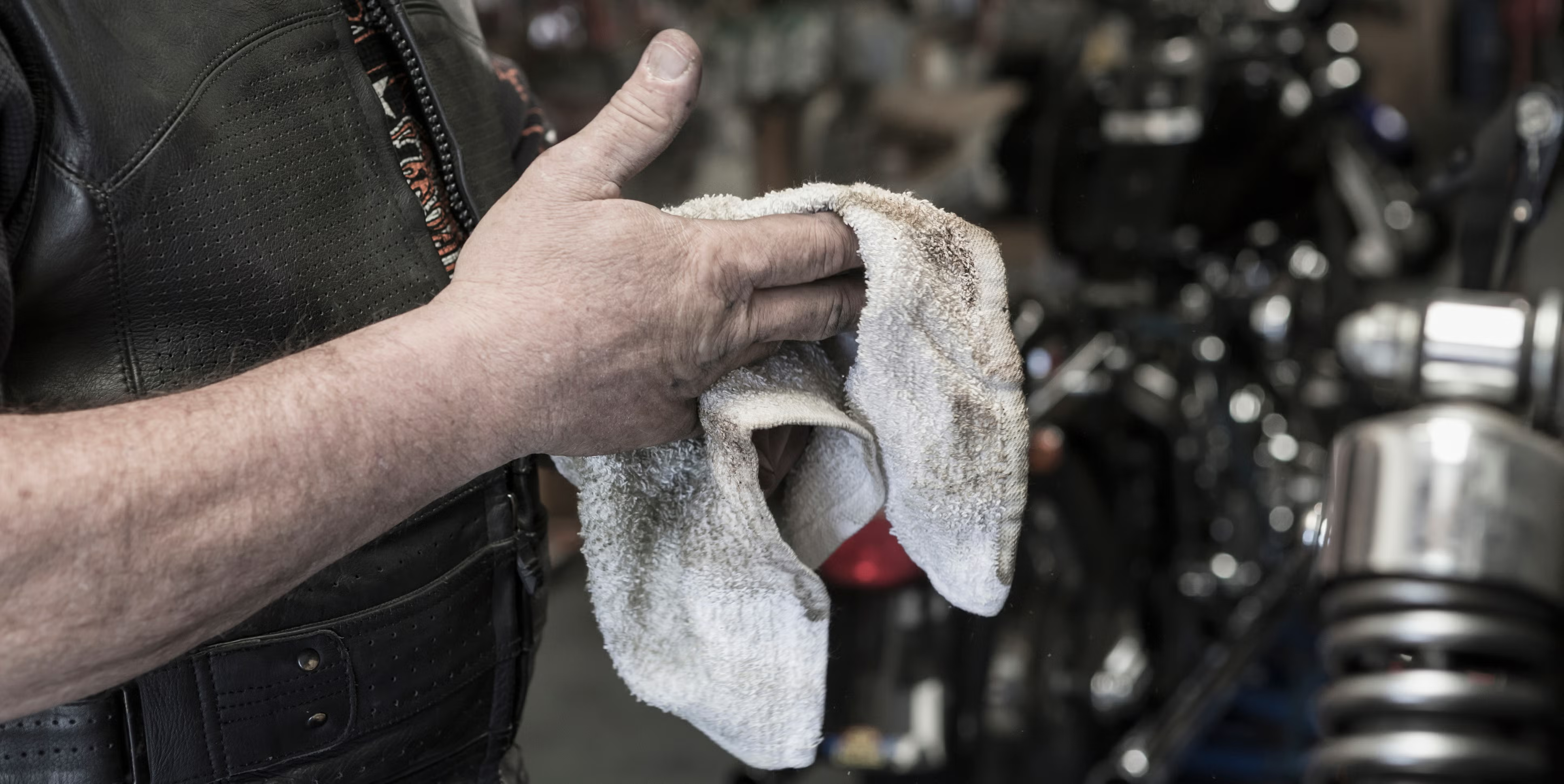 caucasian man repairing motorcycle wiping hands.png